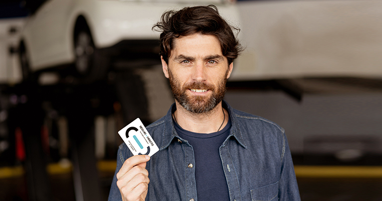 Homem sorridente segura o Cartão de Descontos Seguro Directo numa oficina 